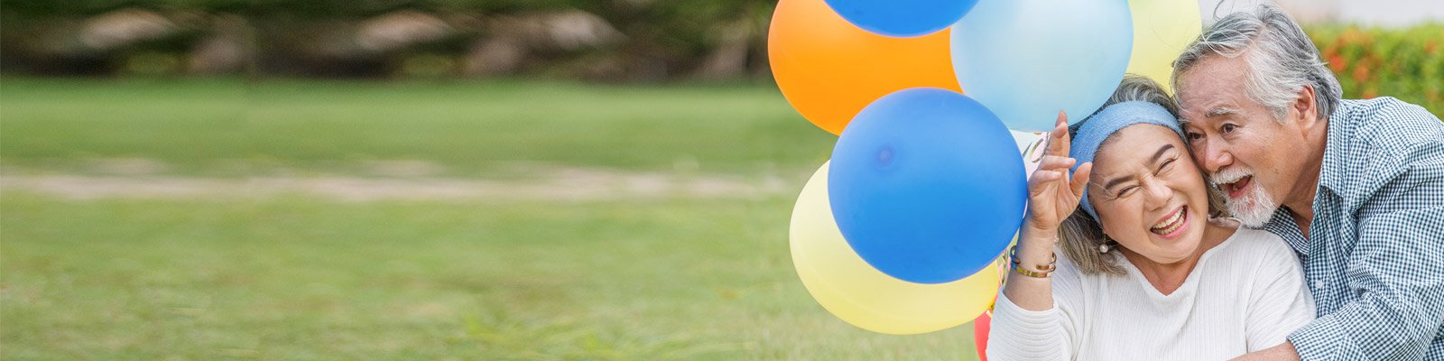 Happy senior couple celebrating with ballons on the front lawn