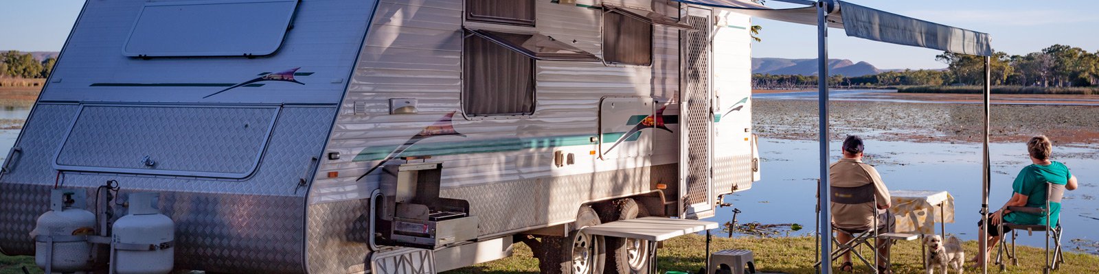 Senior couple with small dog enjoying lake view alongside caravan