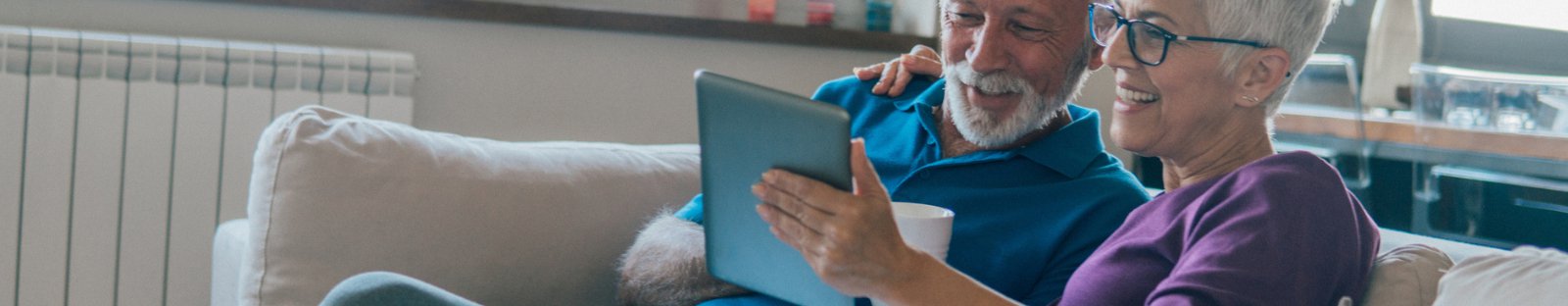 Senior man and woman sitting on couch smiling at tablet