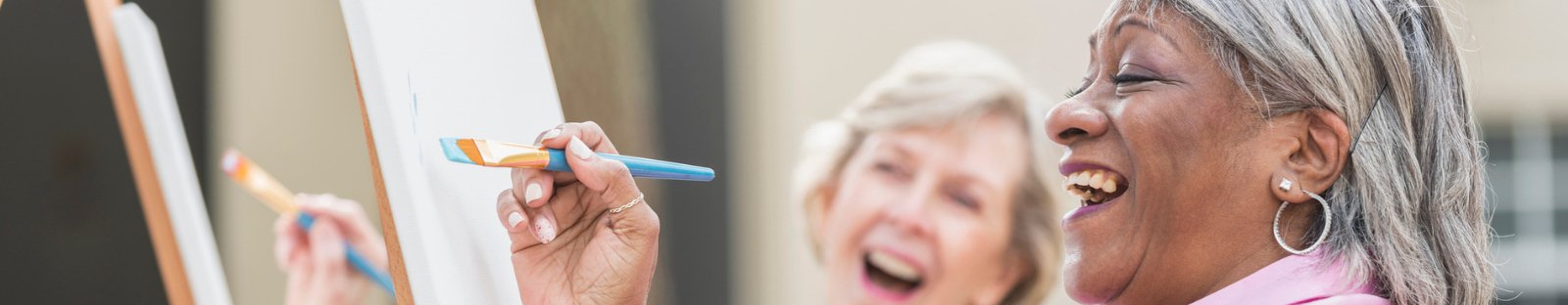 Senior women laughing while painting on canvas